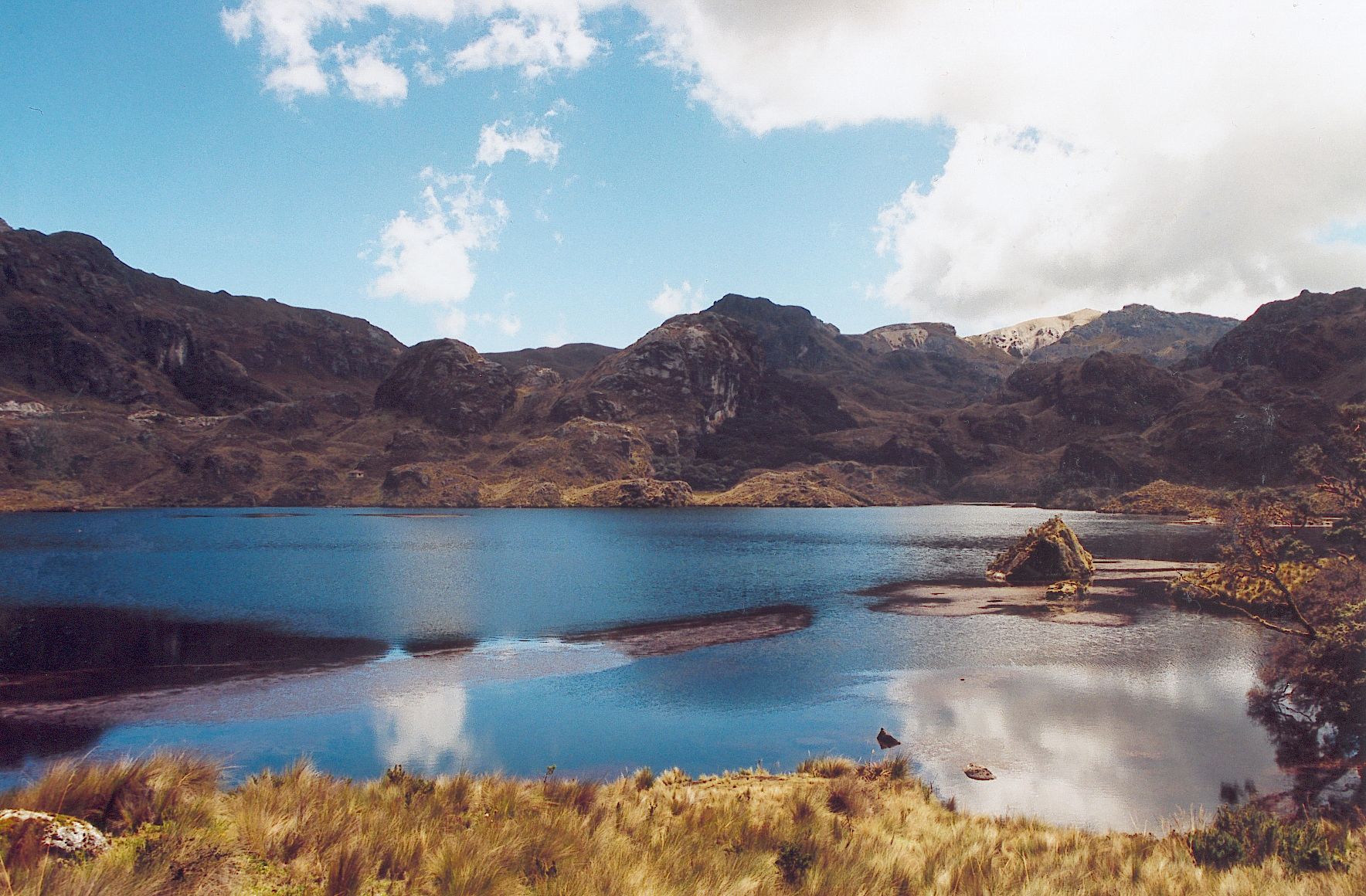 Laguna de aguas azules en el Cajas, entre montañas rocosas y pajonal dorado